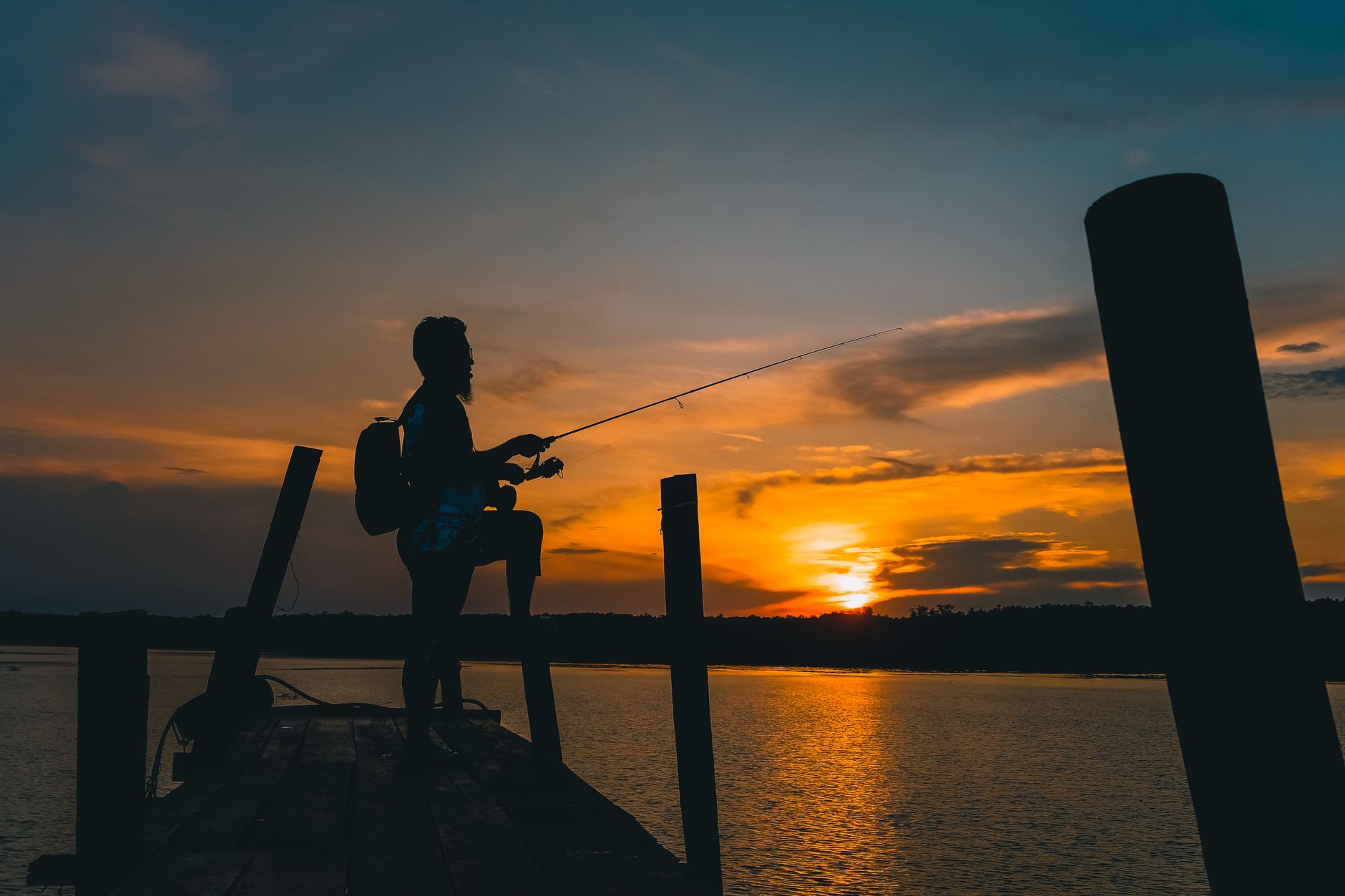 Silhouette d'un pêcheur sur un ponton au coucher du soleil, canne à la main